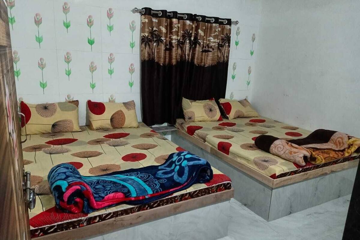 Ein Zimmer mit zwei Einzelbetten, jedes mit einer geblümten Tagesdecke und Kissen. Ein Vorhang mit floralem Muster befindet sich am Fenster.