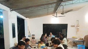 Un grupo de personas cenando en un salón con techos altos e iluminación de estilo industrial.