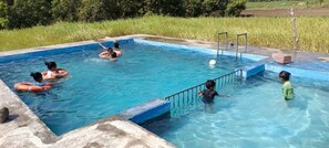 A swimming pool with multiple people, including children and adults, enjoying the water. - S R Farm House (Talala)