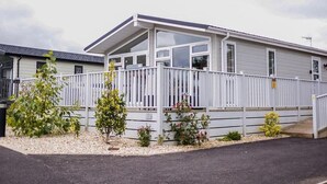 A mobile home with a covered porch, a fenced yard, and a small garden. - Lodge Sleeps 6 with Private Hot Tub (Honiton)