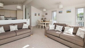 A modern, well-lit living room with two sofas, a dining table, and a kitchen area. - Lodge Sleeps 6 with Private Hot Tub (Honiton)