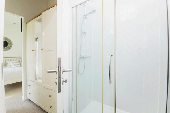 A room with a glass-enclosed shower, a white wardrobe, and a bed with a white headboard. - Lodge Sleeps 6 with Private Hot Tub (Honiton)