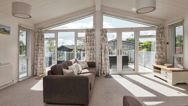 A spacious living room with a large sofa and a smaller couch, a wooden coffee table, and a view of a balcony with a white railing. - Lodge Sleeps 6 with Private Hot Tub (Honiton)
