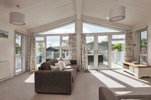 A spacious living room with a large sofa and a smaller couch, a wooden coffee table, and a view of a balcony with a white railing. - Lodge Sleeps 6 with Private Hot Tub (Honiton)