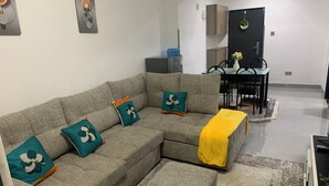 A living room with a grey sectional sofa, matching ottoman, and a patterned rug. - Beautiful 1-Bed Apartment in nairobi (nairobi)