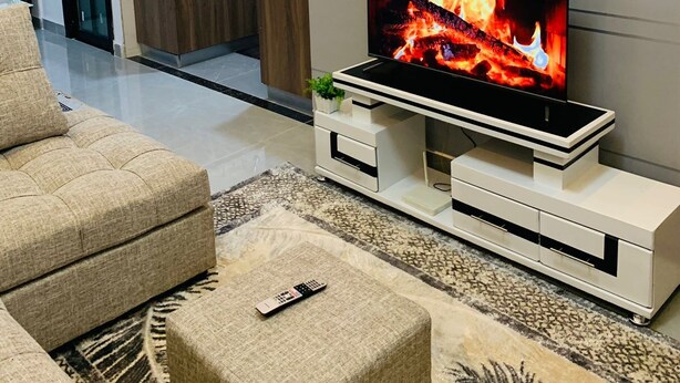 A modern living room with a flat-screen TV displaying a fireplace, a sofa, a coffee table, and a kitchen in the background. - Beautiful 1-Bed Apartment in nairobi (nairobi)