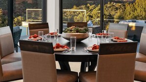 Un coin repas avec une table dressée pour deux personnes, de grandes fenêtres offrant une vue sur un paysage montagneux.