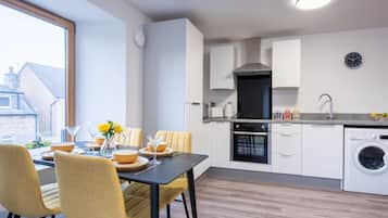 A modern kitchen with a dining area, including a table set for four, chairs, and a view of the outside.