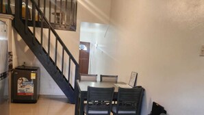 Un soggiorno con un divano dai toni scuri, un tappeto decorato e una scala che conduce a una sala da pranzo con tavolo e sedie.