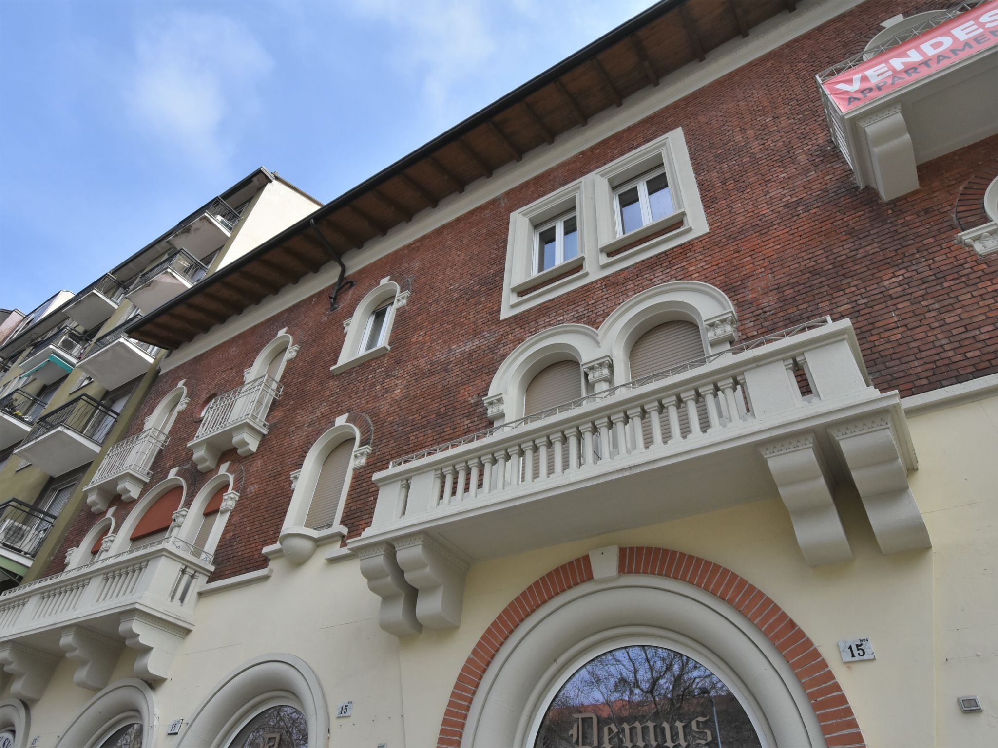 Um edifício com fachada de tijolos vermelhos, detalhes decorativos brancos e uma placa com a inscrição 