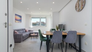 Un salon moderne avec un canapé gris, une table à manger avec quatre chaises, une petite table ronde et une horloge murale.