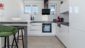 Une cuisine moderne avec des meubles blancs, un four encastré, une machine à café et un tabouret de bar vert.