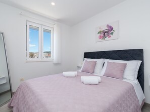 Une chambre à coucher avec un lit, des oreillers, une fenêtre et une œuvre d’art accrochée au mur.