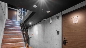 A staircase leading to a second floor with a wooden finish, a dark ceiling with recessed lighting, and a wooden door with a lock. - SERAPHIC 101 (Chitose)