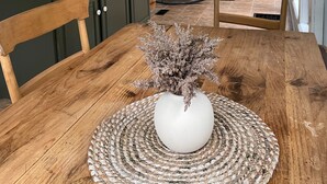 Un tavolo da pranzo in legno con un vaso bianco al centro, circondato da sedie.