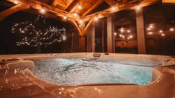 Una vasca idromassaggio in una baita di legno con soffitto alto e luci a stringa.
