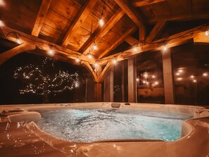 A hot tub in a wooden cabin with a high ceiling and string lights.