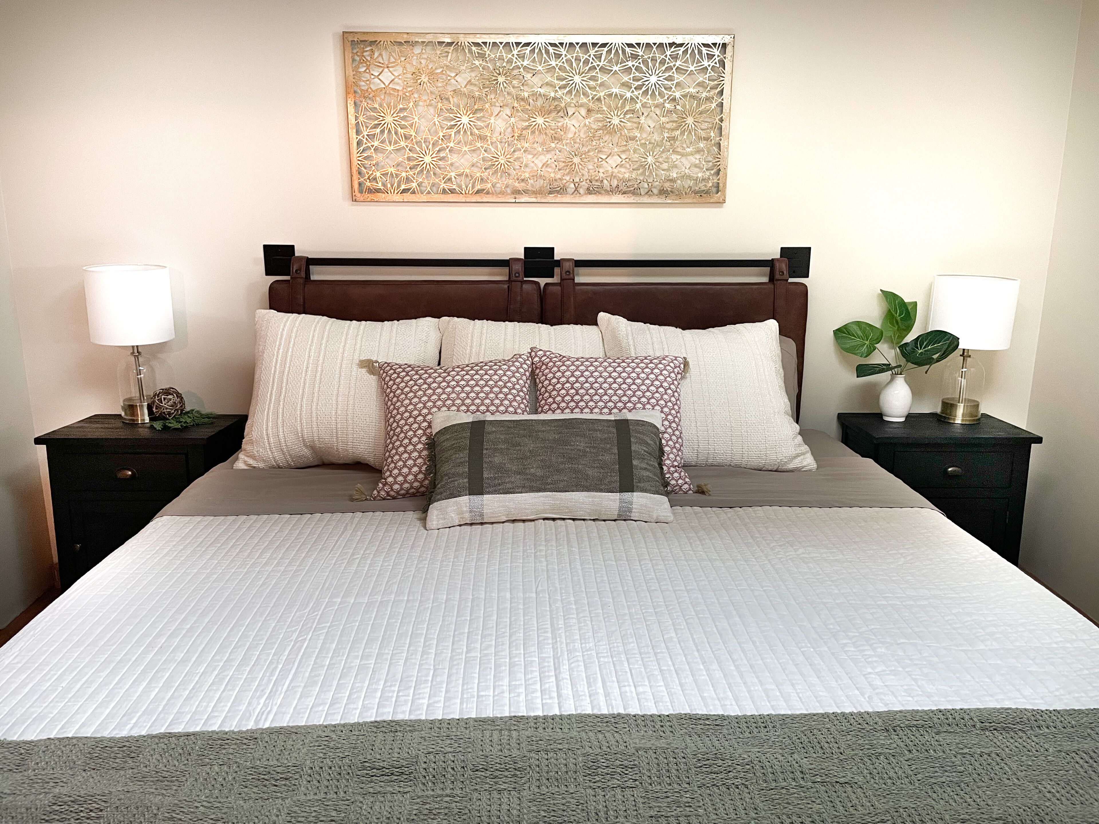 A neatly made bed with a patterned bedspread, multiple pillows, and two bedside tables with lamps and decorative items.