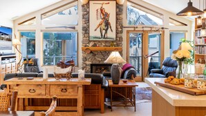 Un salon spacieux doté d’une cheminée en pierre, de meubles en bois et de grandes fenêtres offrant une vue sur l’extérieur.