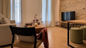 A modern living room with a sofa, a coffee table, a TV, and a stone wall. - Redes Royale Apartments ·B1· by Misterhost (Sevilla)