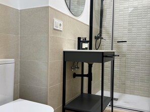 A modern bathroom with a toilet, a shower area, and a sink with a black countertop.