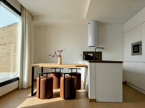 Eine moderne Küche mit einem Holzesstisch, drei Hocker, einer Vase mit Blumen und einer eingebauten Mikrowelle.