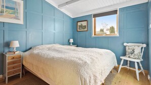Une chambre à coucher avec un grand lit, deux tables de chevet avec des lampes, une chaise et une fenêtre donnant sur des arbres.