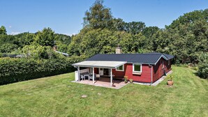 Une maison rouge avec un patio couvert et une cheminée, entourée d’une végétation luxuriante.