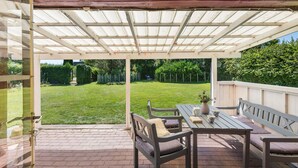 Un patio couvert avec un sol en briques, des meubles en bois et une vue sur une cour verdoyante.
