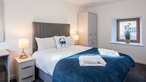 Un dormitorio ordenado con cama, mesitas de noche, armario y ventana con planta.