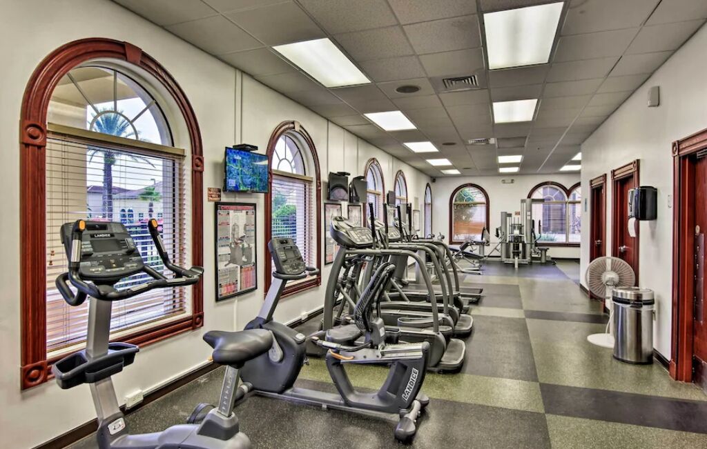 Une salle de sport équipée de nombreux appareils de cardio, dotée de grandes fenêtres et d’un sol à carreaux.