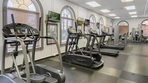 Un gimnasio con cintas de correr y elípticas, ventanas amplias con persianas y un diseño moderno y cuidado.