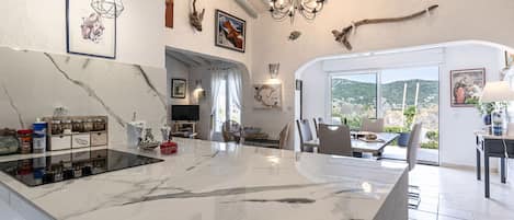A spacious kitchen with a marble island, modern pendant lights, and a large window offering a view of the outdoors.