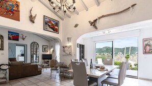 A spacious living area with a dining table, comfortable seating, and a large window offering a scenic view. - Vacation home Paulka by Interhome (Sainte Lucie Porto Vecchio)