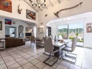 Relax in this stylish living area with a dining table, sofa, and TV, surrounded by artwork and a large window with a scenic view.