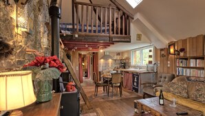 Un intérieur chaleureux et rustique, avec un escalier en bois, un coin cuisine et un espace salon comprenant un canapé et une table.