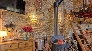 Un intérieur rustique avec un mur en pierre, un meuble en bois, un vase rempli de fleurs rouges, une horloge murale et un poêle à bois.