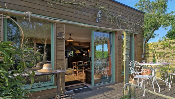Une terrasse en bois avec des sièges extérieurs et une porte vitrée donnant sur un espace intérieur.