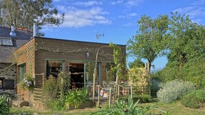 Une maison rustique en bois, dotée d’un jardin à l’avant, avec un mur en pierre, une clôture en bois et diverses plantes.