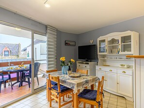 A dining area with a table set for two, a television, and a cabinet with glass doors. - Le Nautilus by Interhome (Locmariaquer)