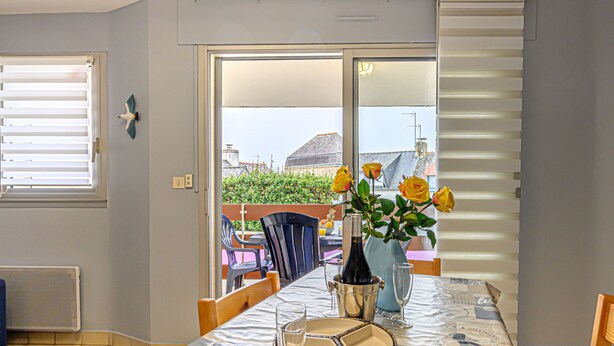 Ein Essbereich mit einem Tisch für zwei Personen, einer Vase mit gelben Blumen und Blick auf die Stadt durch das Fenster.