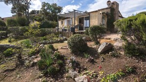 Un bâtiment rustique en pierre, doté d’un patio et entouré de diverses plantes et arbres.