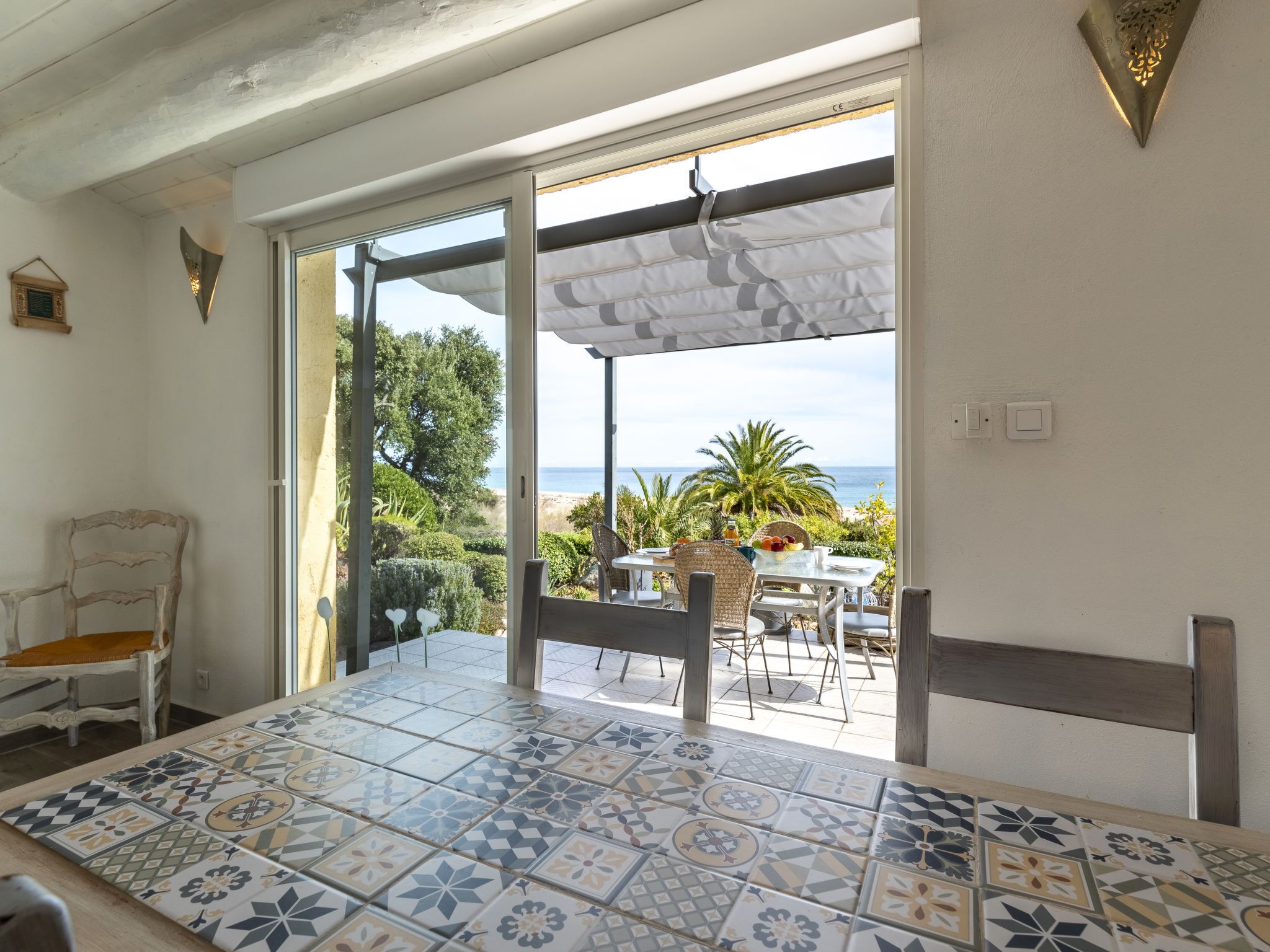 Quarto com piso de azulejos, mesa com cadeiras e vista para a praia, com porta que dá para o exterior.