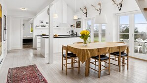 A spacious kitchen with a central island, a dining area with a table and chairs, and a view of the outdoors through large windows. - "Marrit" - 500m from the sea by Interhome (Glesborg)