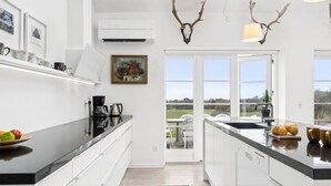 A modern kitchen with white cabinets, a black countertop, and a view of the outdoors through large windows. - "Marrit" - 500m from the sea by Interhome (Glesborg)