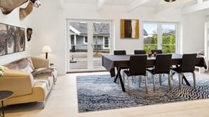 A modern dining area with a table set for four, surrounded by chairs, in a bright room with a large window and a view of a house. - "Marrit" - 500m from the sea by Interhome (Glesborg)