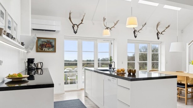 A modern kitchen with white cabinetry, a central island, and pendant lights with antler decorations. - "Marrit" - 500m from the sea by Interhome (Glesborg)