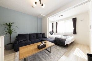 A modern living room with a sofa, a wooden coffee table, a potted plant, and a large window with curtains. - SECLUSION Chitose MS102 (Chitose)