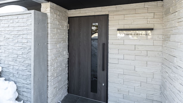 Una entrada moderna con una puerta de madera oscura, paredes de piedra blanca y un letrero sobre la puerta.