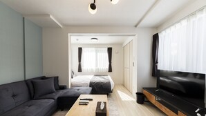 Una sala moderna con un sofá, una mesa de centro, un televisor y un dormitorio al fondo.